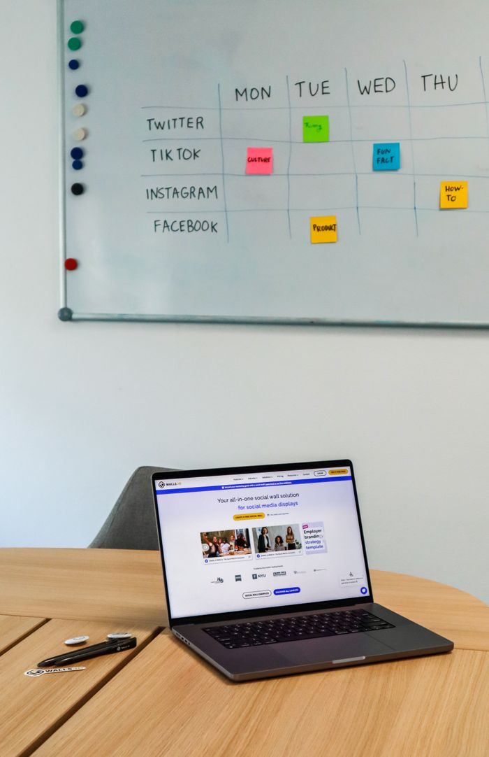 about-04 A contemporary office arrangement with a laptop and a whiteboard timetable for social media platforms.